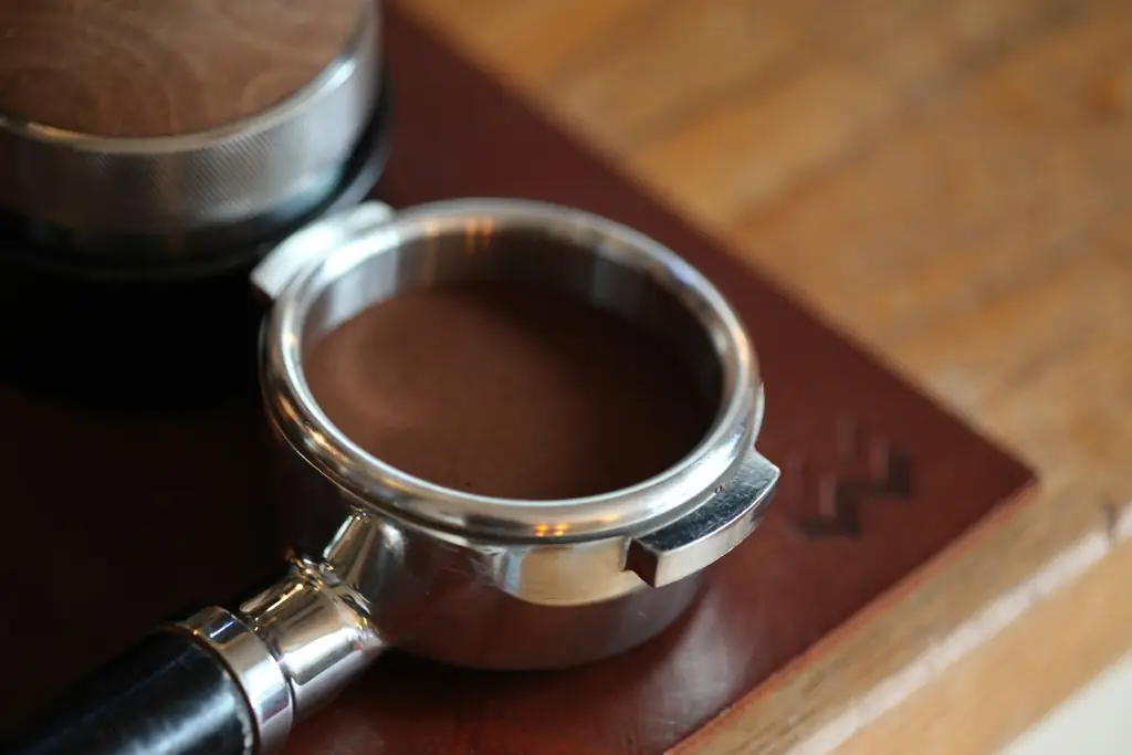 Portafilter filled with freshly ground coffee on a leather tamping mat