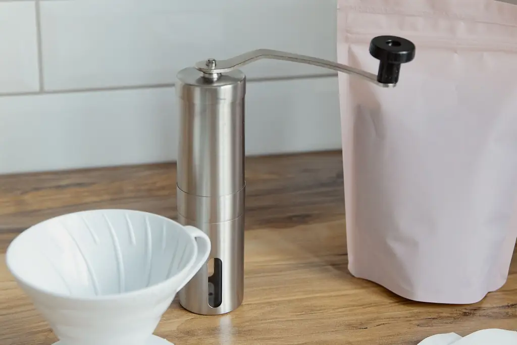 Stainless steel hand coffee grinder with a crank on a kitchen counter (illustrative, not a specific model)