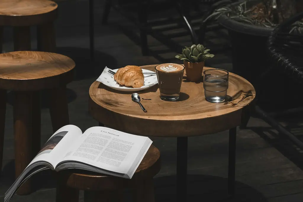A latte, a croissant and an open book on a café table