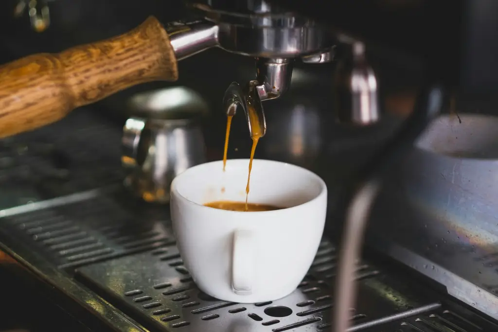 Espresso running from a wooden-handled portafilter into a white cup
