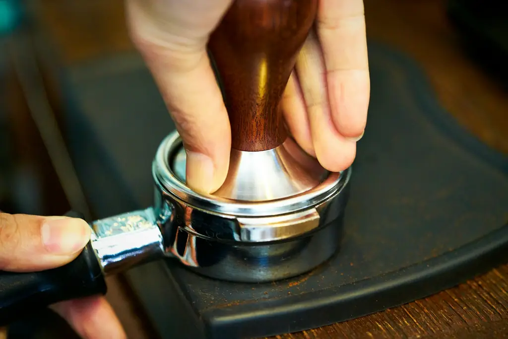 Tamping ground coffee in a portafilter with a wooden-handled tamper